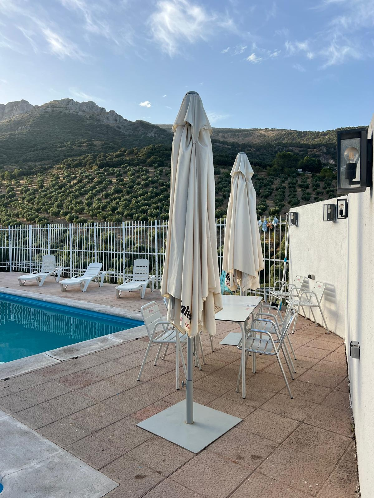 Zona de sombrillas y mesas junto a la piscina con vistas al campo