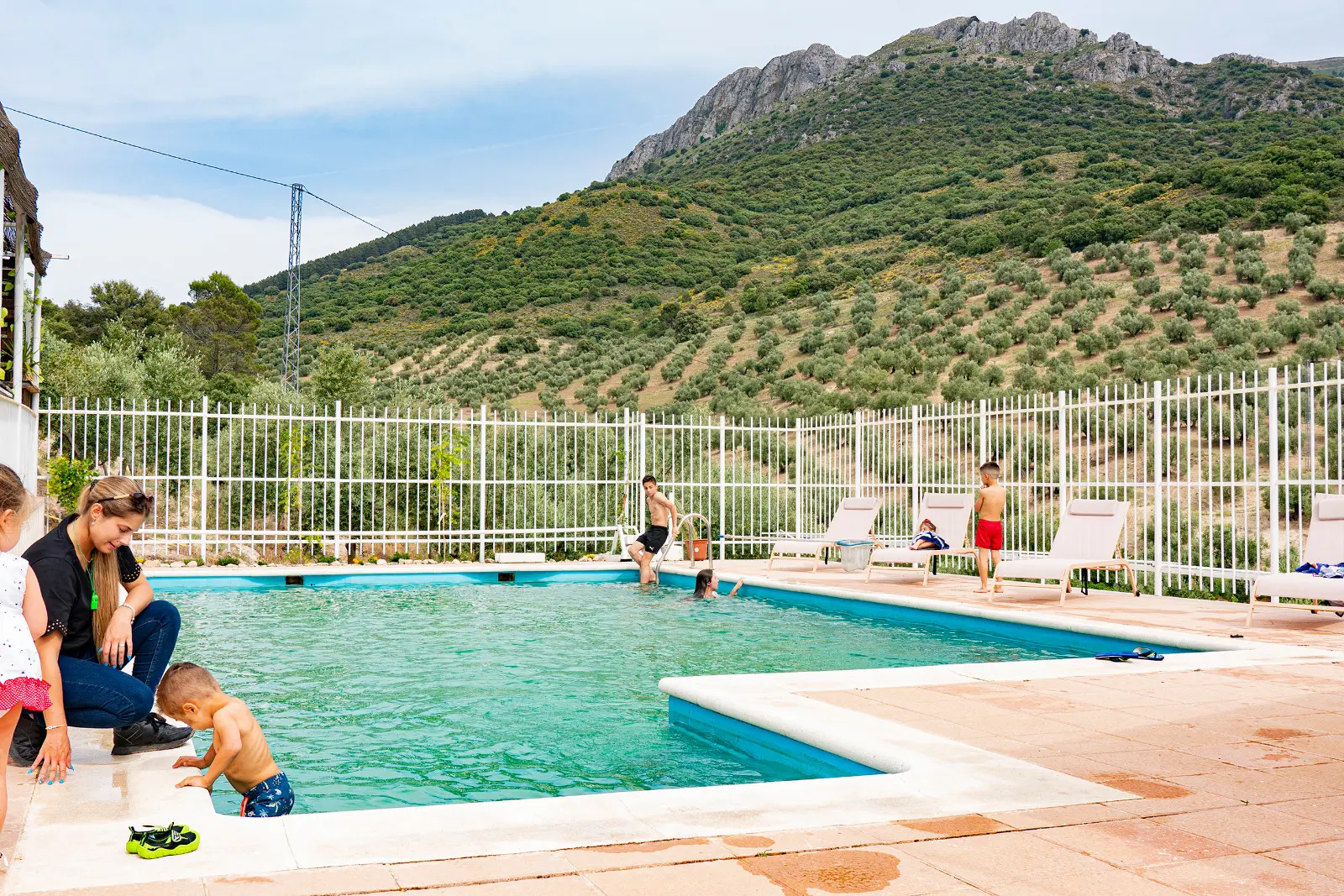 Piscina de Villa de Dulce con familias bañándose y la sierra de olivos al fondo